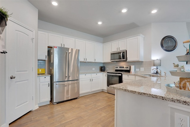 kitchen with light wood-type flooring, light stone counters, white cabinets, sink, and appliances with stainless steel finishes