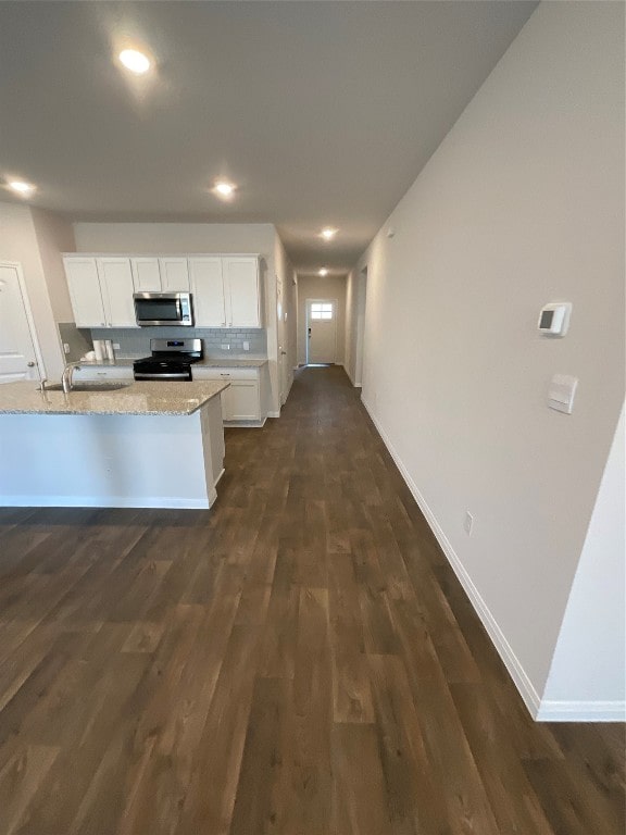 kitchen with light stone counters, dark hardwood / wood-style flooring, stainless steel appliances, and white cabinets