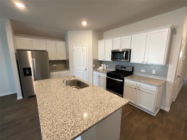 kitchen featuring light stone counters, stainless steel appliances, sink, white cabinetry, and a center island with sink