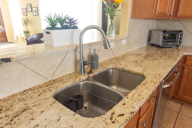 kitchen with dishwasher, backsplash, sink, light tile patterned floors, and light stone counters