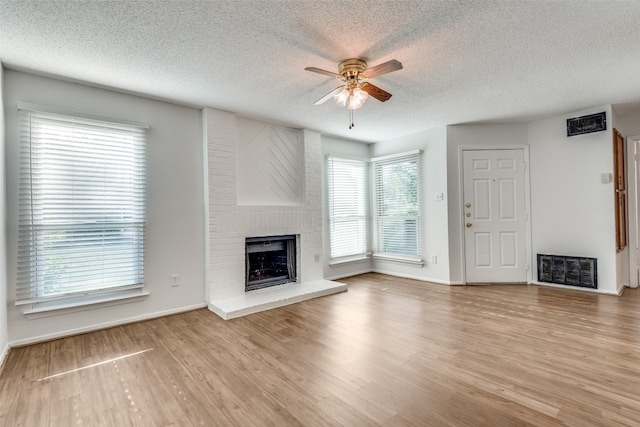 unfurnished living room featuring a fireplace, ceiling fan, light wood-type flooring, and a textured ceiling