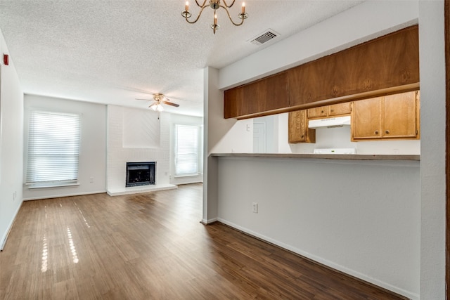 kitchen with ceiling fan with notable chandelier, a fireplace, dark wood-type flooring, and kitchen peninsula