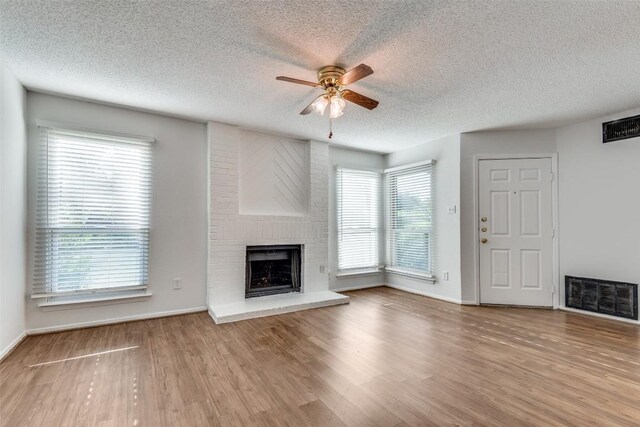 10616 Mellow Mdws Unit 9D, Austin, TX 78750 - unfurnished living room with a ceiling fan, wood finished floors, a textured ceiling, a fireplace, and visible vents