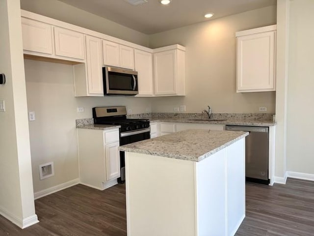 kitchen featuring dark wood finished floors, stainless steel appliances, white cabinetry, a kitchen island, and a sink