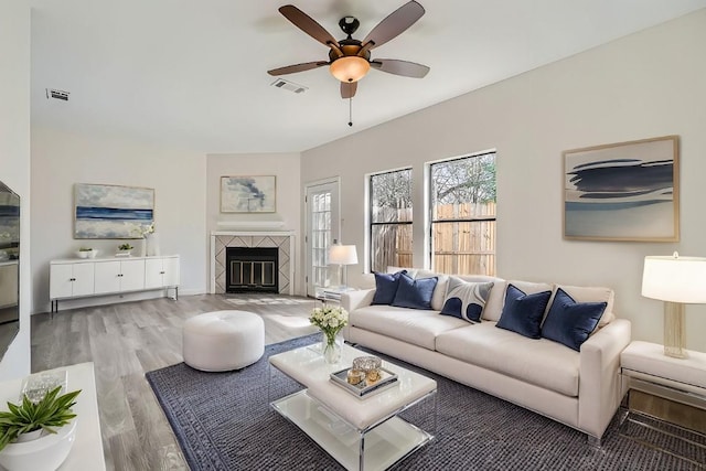 living room with a ceiling fan, a fireplace, visible vents, and wood finished floors