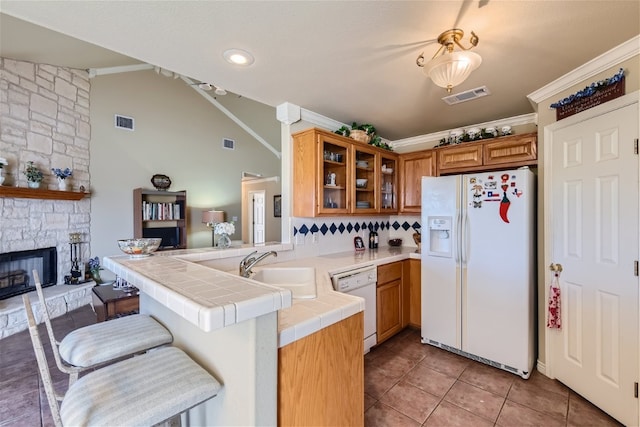 kitchen with tile countertops, kitchen peninsula, sink, white appliances, and a kitchen bar