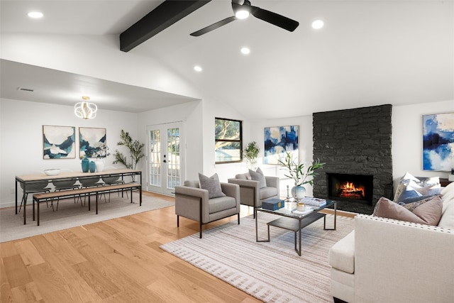 living room featuring french doors, light wood-type flooring, ceiling fan, beamed ceiling, and a stone fireplace