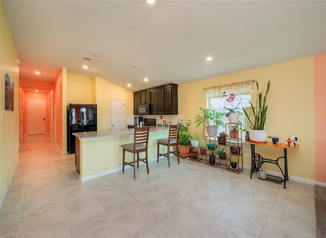 kitchen with a breakfast bar area, vaulted ceiling, light stone countertops, kitchen peninsula, and black appliances