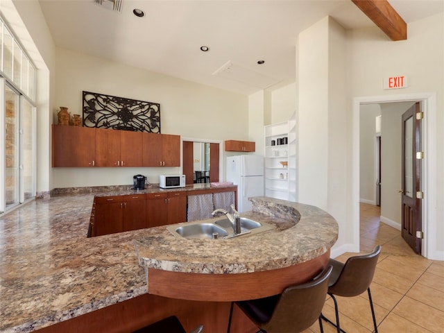 kitchen featuring white appliances, a breakfast bar, sink, kitchen peninsula, and light tile patterned floors