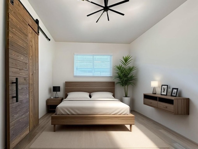 bedroom with a barn door, ceiling fan, and light wood-type flooring