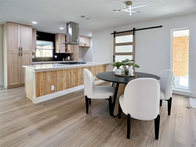 kitchen featuring light brown cabinets, a barn door, light hardwood / wood-style flooring, stainless steel gas stovetop, and island range hood