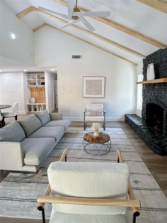 living room featuring ceiling fan, wood-type flooring, beam ceiling, high vaulted ceiling, and a stone fireplace