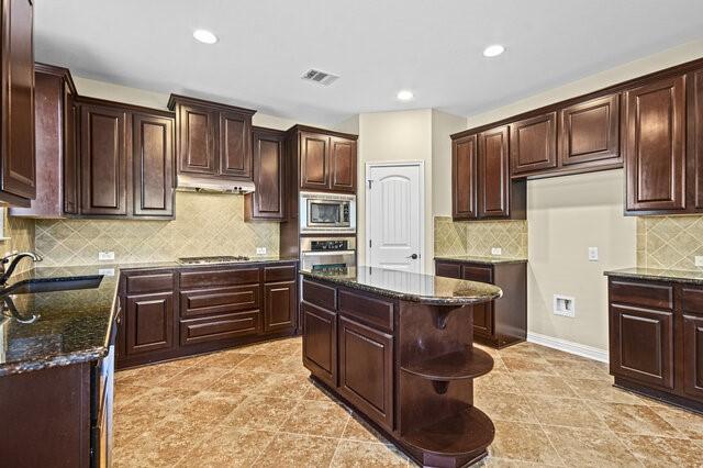 kitchen with sink, a center island, dark stone countertops, appliances with stainless steel finishes, and decorative backsplash