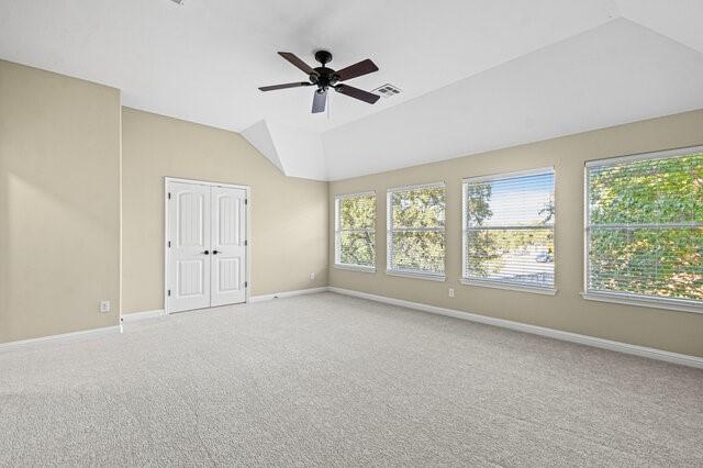 carpeted empty room featuring ceiling fan, vaulted ceiling, and a healthy amount of sunlight