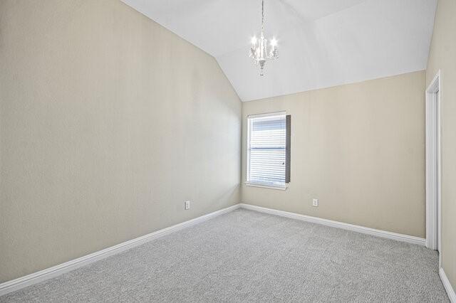 carpeted spare room with vaulted ceiling and an inviting chandelier