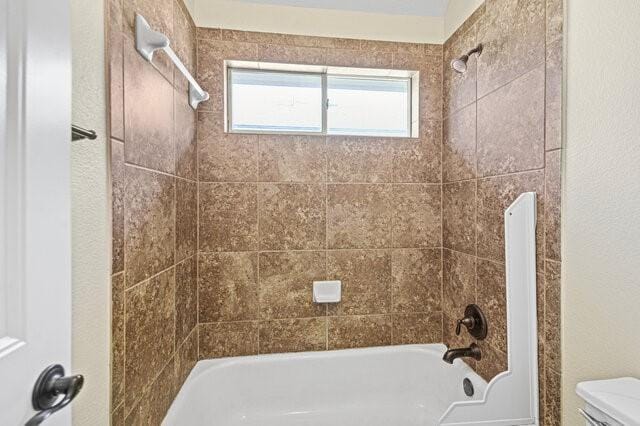 bathroom featuring tiled shower / bath combo and toilet