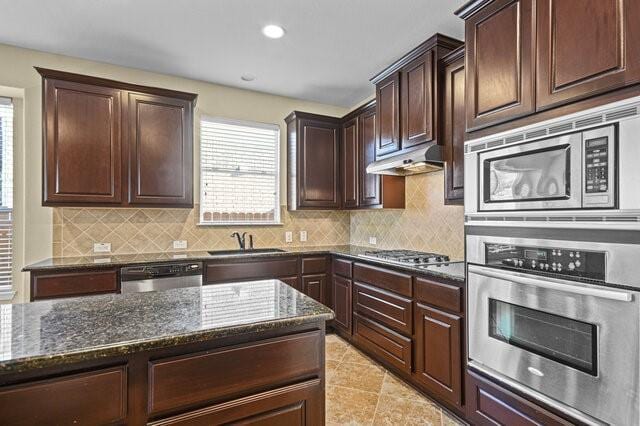 kitchen with appliances with stainless steel finishes, sink, backsplash, dark stone counters, and dark brown cabinetry