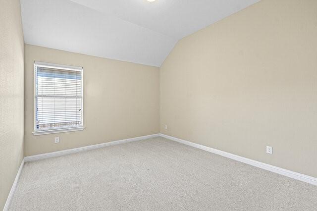 spare room featuring light carpet and vaulted ceiling