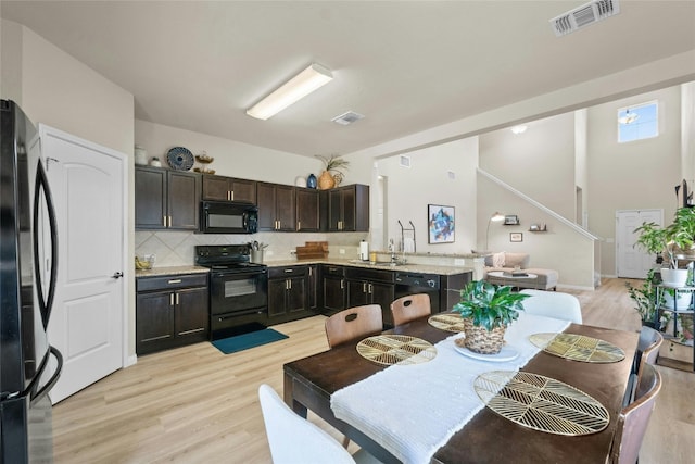 kitchen featuring tasteful backsplash, black appliances, dark brown cabinetry, and light wood-type flooring