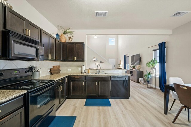 kitchen with light stone counters, black appliances, sink, and light wood-type flooring