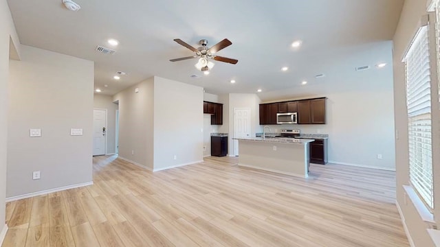 kitchen with ceiling fan, light wood-type flooring, a kitchen island with sink, appliances with stainless steel finishes, and light stone countertops