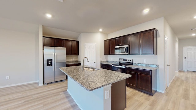 kitchen with stainless steel appliances, a center island with sink, sink, light stone countertops, and light hardwood / wood-style floors