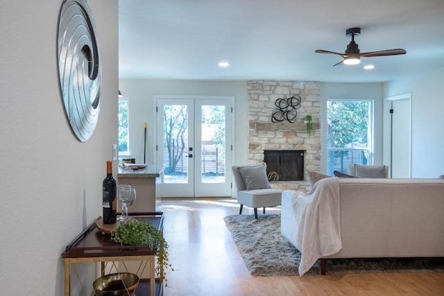 living room featuring french doors, ceiling fan, a fireplace, and light wood-type flooring