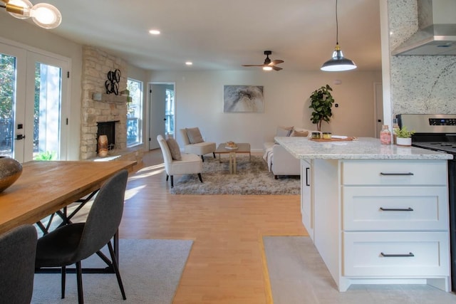 kitchen featuring stainless steel electric range oven, decorative light fixtures, white cabinets, light stone counters, and wall chimney exhaust hood