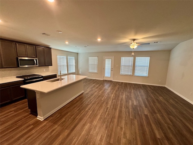 kitchen with black range, an island with sink, dark brown cabinets, ceiling fan, and dark hardwood / wood-style floors