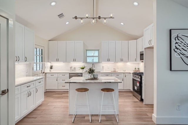 kitchen with light stone counters, light hardwood / wood-style flooring, white cabinetry, stainless steel appliances, and a center island