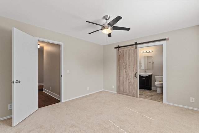 unfurnished bedroom with ensuite bathroom, sink, a barn door, ceiling fan, and carpet