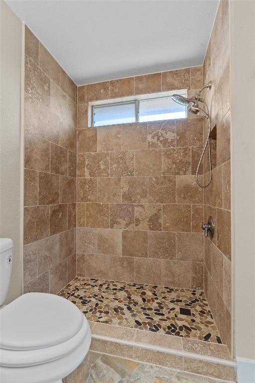 bathroom with toilet, tiled shower, and plenty of natural light