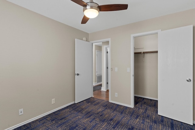 unfurnished bedroom featuring dark carpet, a walk in closet, a closet, and ceiling fan