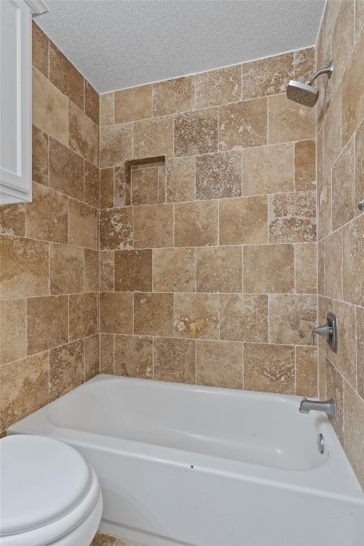 bathroom with toilet, tiled shower / bath combo, and a textured ceiling