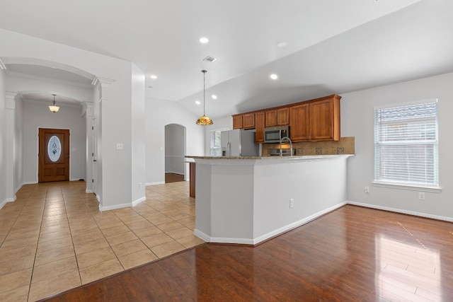 kitchen with lofted ceiling, kitchen peninsula, appliances with stainless steel finishes, pendant lighting, and light hardwood / wood-style floors