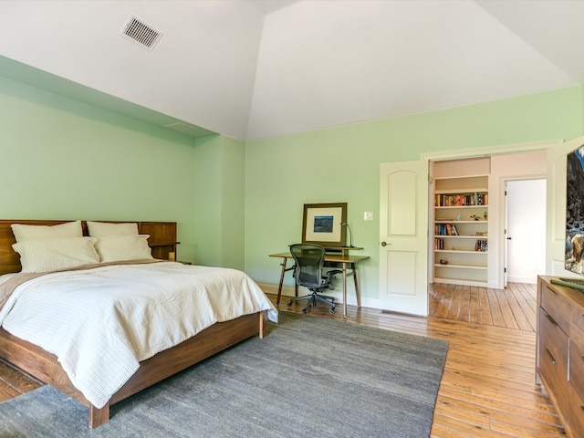 bedroom featuring a walk in closet, wood-type flooring, and vaulted ceiling