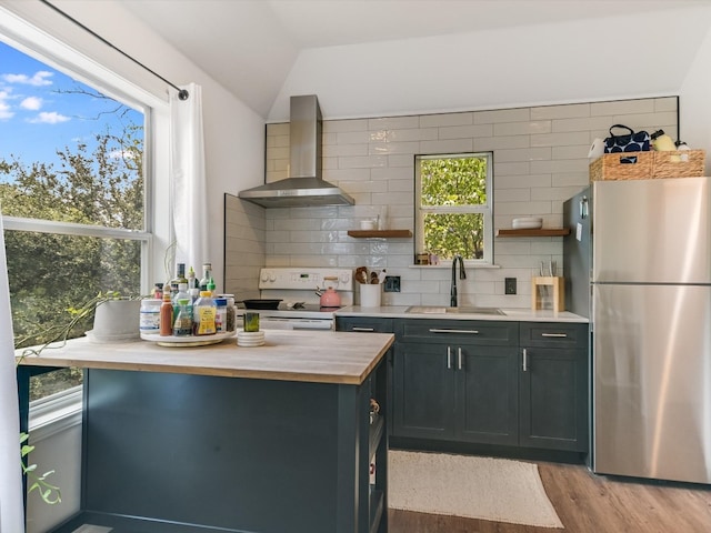 kitchen featuring sink, wall chimney range hood, backsplash, stainless steel fridge, and stove