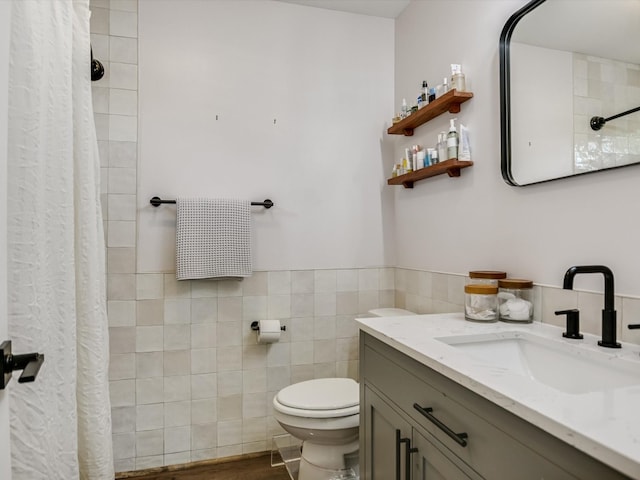 bathroom featuring walk in shower, vanity, toilet, and tile walls