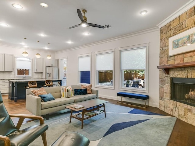 living room featuring ornamental molding, ceiling fan, sink, hardwood / wood-style floors, and a stone fireplace