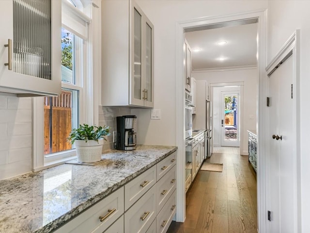 kitchen featuring white cabinets, a healthy amount of sunlight, light stone countertops, and crown molding