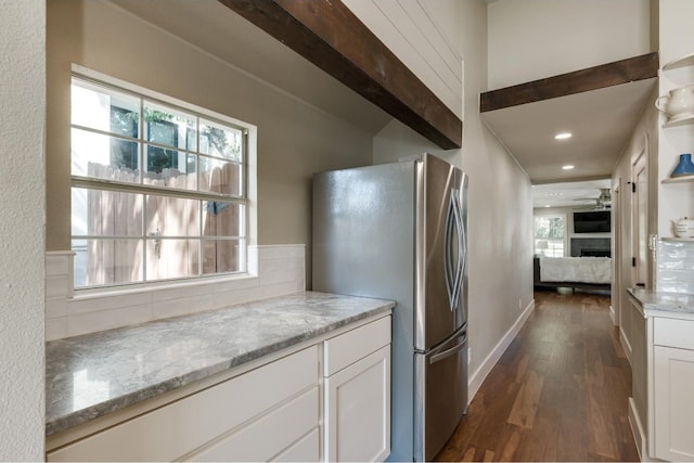 kitchen with light stone counters, a healthy amount of sunlight, stainless steel refrigerator, and white cabinets