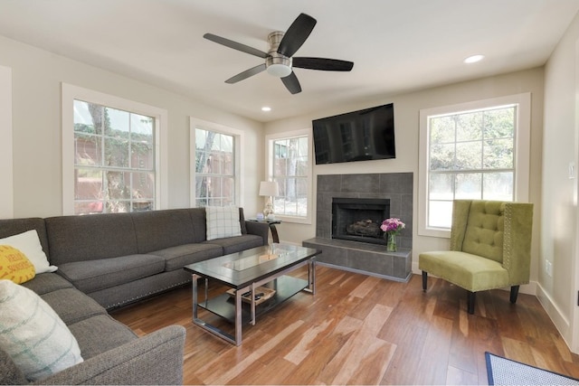 living room featuring ceiling fan, a tile fireplace, hardwood / wood-style floors, and a healthy amount of sunlight