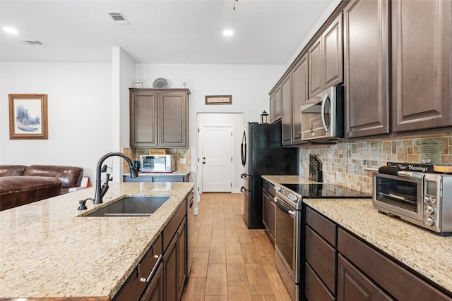 kitchen featuring appliances with stainless steel finishes, sink, dark brown cabinetry, light stone counters, and light hardwood / wood-style flooring