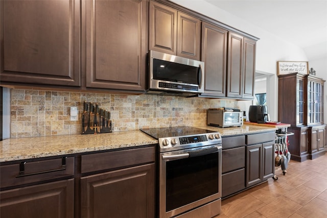 kitchen featuring light stone counters, appliances with stainless steel finishes, dark brown cabinetry, and backsplash