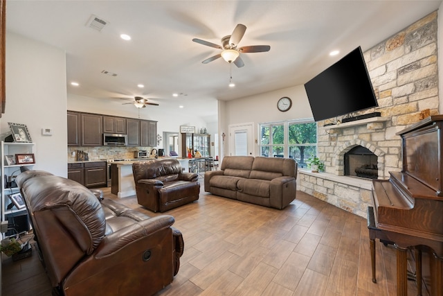 living room with a stone fireplace, light hardwood / wood-style flooring, and ceiling fan