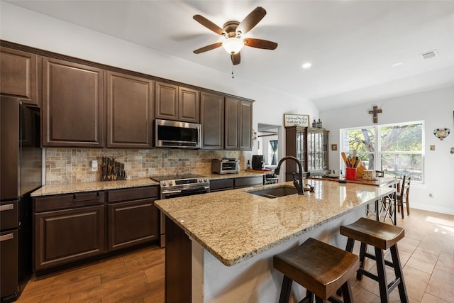 kitchen with an island with sink, appliances with stainless steel finishes, a breakfast bar area, dark brown cabinetry, and sink