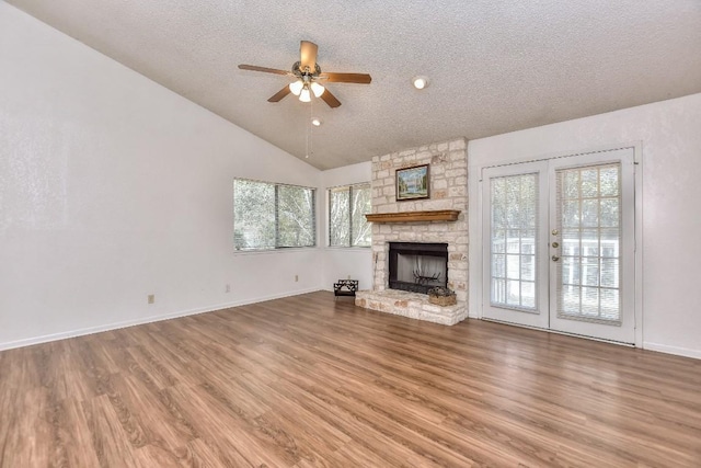 unfurnished living room with ceiling fan, a stone fireplace, vaulted ceiling, a textured ceiling, and hardwood / wood-style flooring