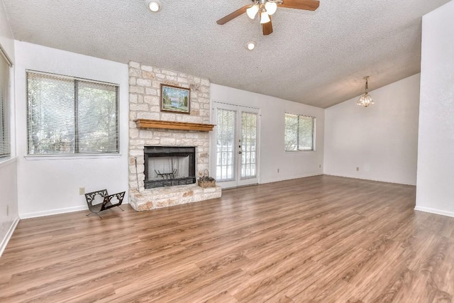 unfurnished living room with ceiling fan with notable chandelier, hardwood / wood-style floors, a textured ceiling, and a stone fireplace