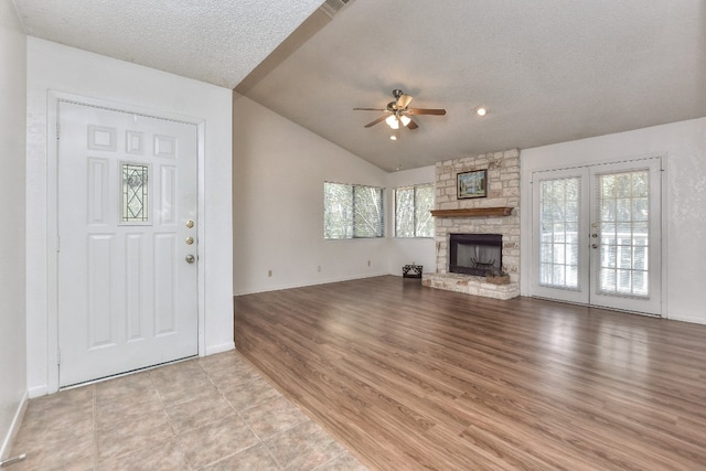 unfurnished living room with ceiling fan, a stone fireplace, a textured ceiling, and vaulted ceiling