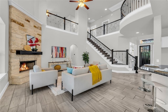 living room with light hardwood / wood-style floors, a stone fireplace, a high ceiling, and ceiling fan